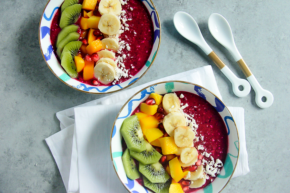 Tropical smoothie bowl topped with dragon fruit, mango, strawberries, granola, and coconut.