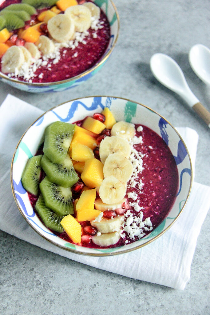 Tropical smoothie bowl topped with dragon fruit, mango, strawberries, granola, and coconut.