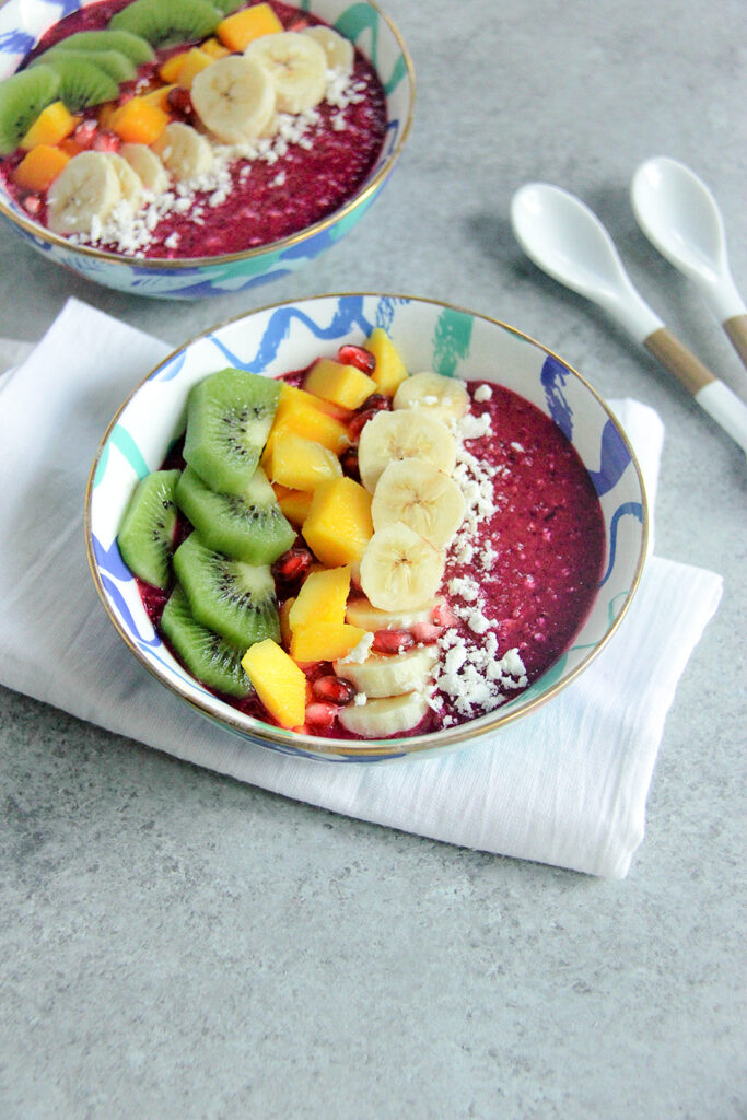 Tropical smoothie bowl topped with dragon fruit, mango, strawberries, granola, and coconut.