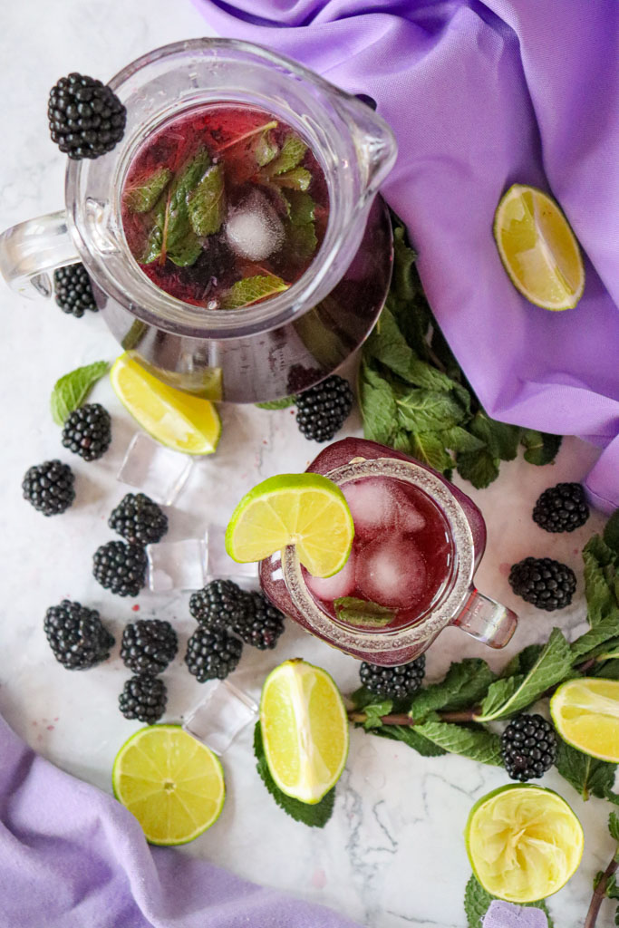 Summer-ready drink scene with a glass of blackberry lemon mocktail, ice cubes glistening, and fresh blackberries scattered around.