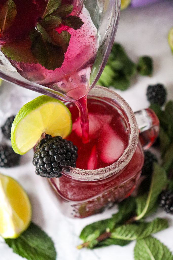 A tall glass of blackberry lemon mocktail with sparkling fizz, fresh mint, lime slices, and whole blackberries for garnish.