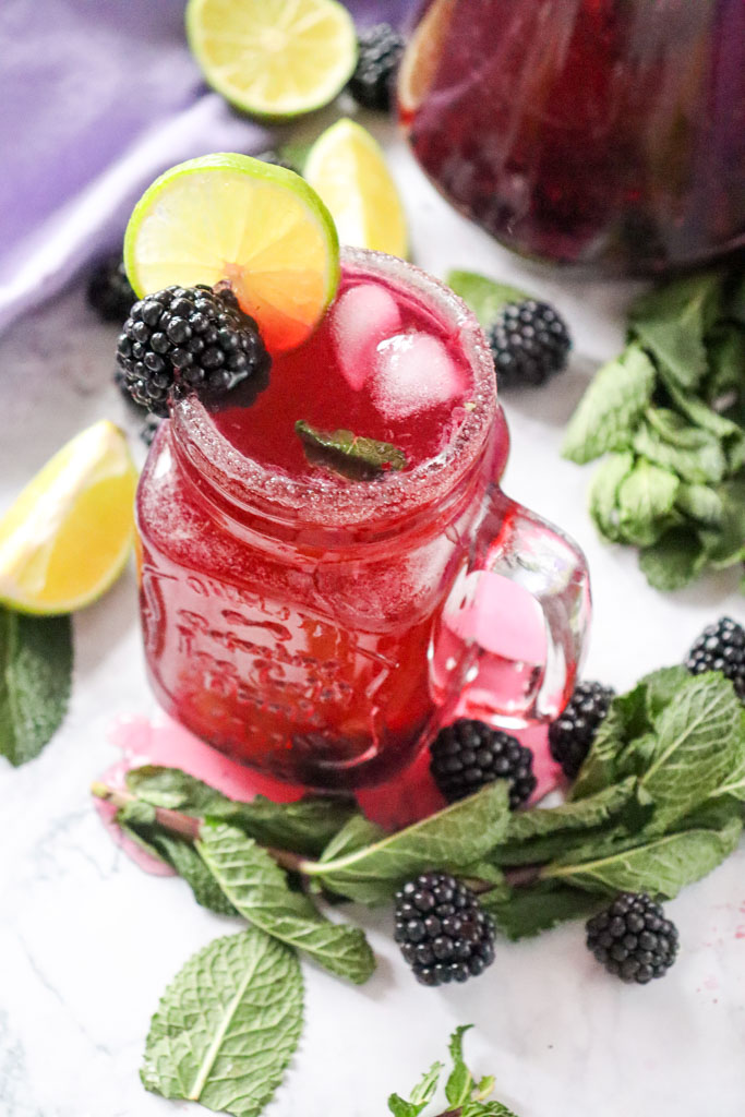 A tall glass of blackberry lemon mocktail with sparkling fizz, fresh mint, lime slices, and whole blackberries for garnish.