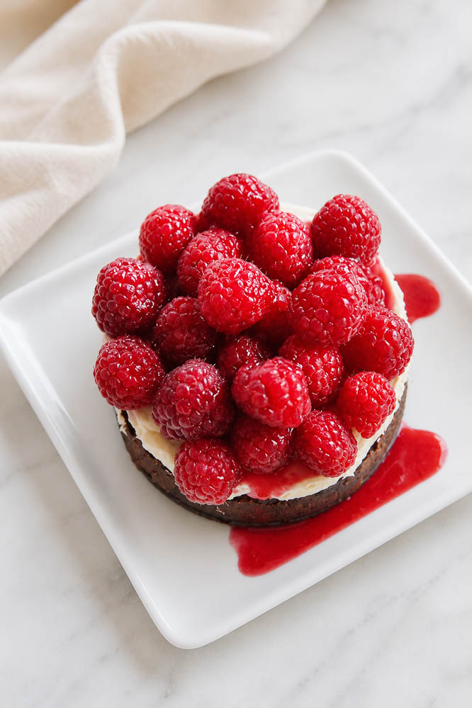 This Bloody Halloween Cheesecake has a chocolate crust, creamy no-bake filling, fresh raspberries, and raspberry “blood” sauce with food-safe syringes.