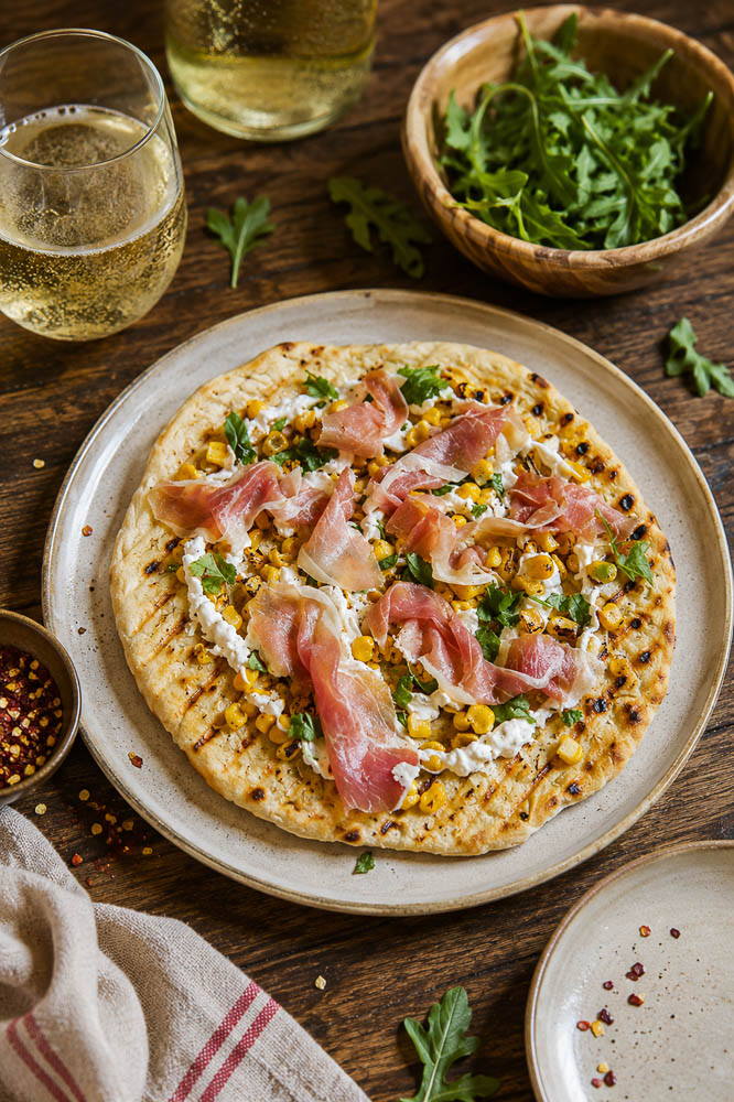 This Roasted Corn Pizza with Cilantro Lime Sauce combines sweet, lightly charred corn with melty mozzarella, salty prosciutto, and a creamy cilantro lime sauce for a homemade pizza that feels fresh, colorful, and a little unexpected.