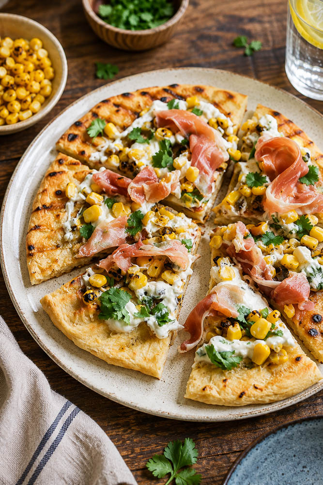 This Roasted Corn Pizza with Cilantro Lime Sauce combines sweet, lightly charred corn with melty mozzarella, salty prosciutto, and a creamy cilantro lime sauce for a homemade pizza that feels fresh, colorful, and a little unexpected.