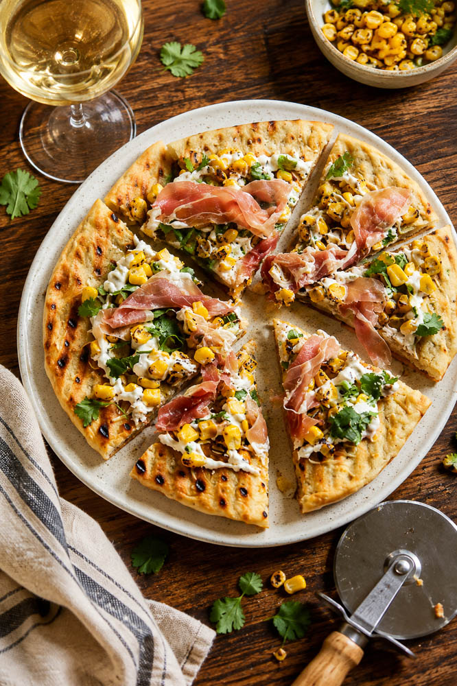 This Roasted Corn Pizza with Cilantro Lime Sauce combines sweet, lightly charred corn with melty mozzarella, salty prosciutto, and a creamy cilantro lime sauce for a homemade pizza that feels fresh, colorful, and a little unexpected.